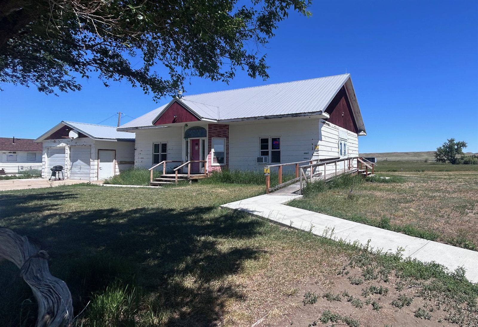 Highline Apothecary's white building at 12 Porcupine Ln in Nashua, Montana, on a sunny day: a red front door, front steps and a wheelchair ramp leading to the entrance