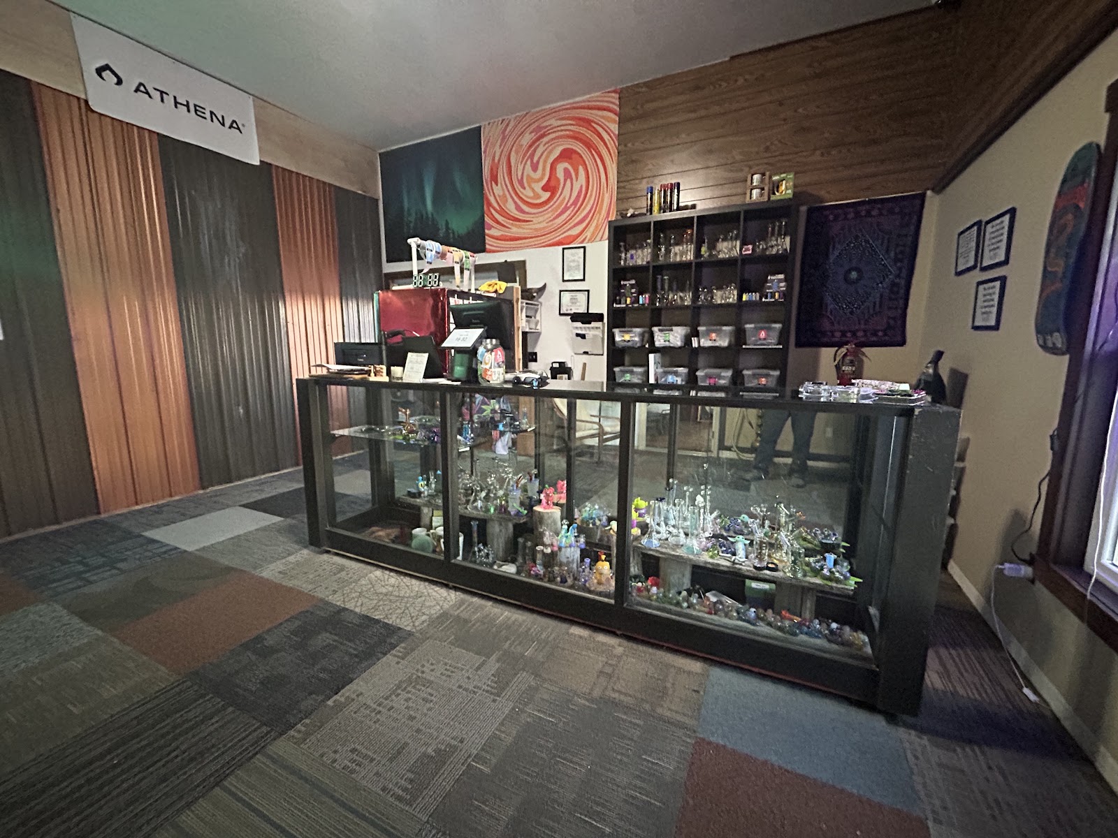 Inside Highline Apothecary: a long glass display case of pipes and glass, wood-panelled walls, and painted canvases above the counter
